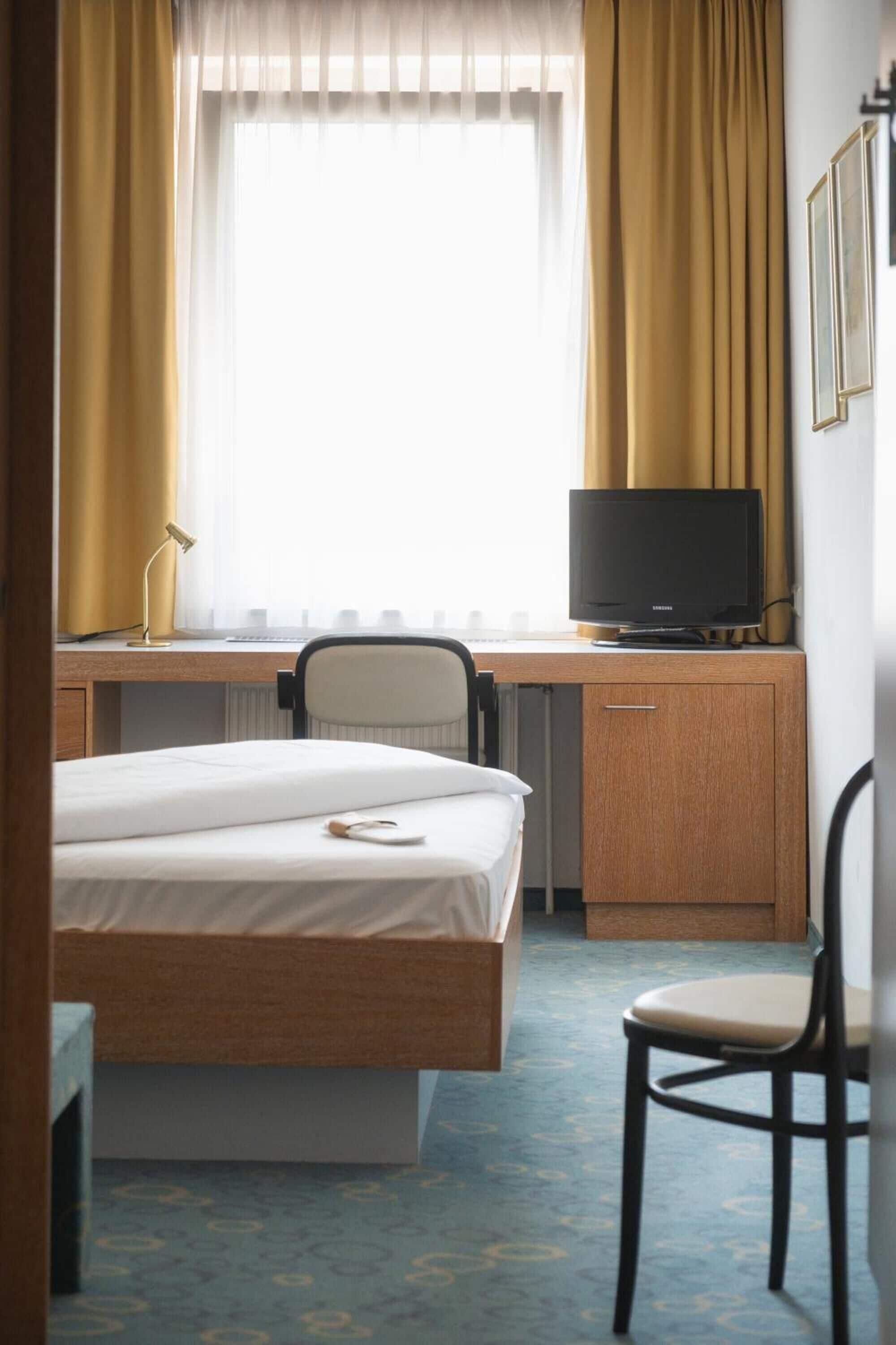 Habitación de hotel con cama, escritorio, silla, televisor y cortinas.