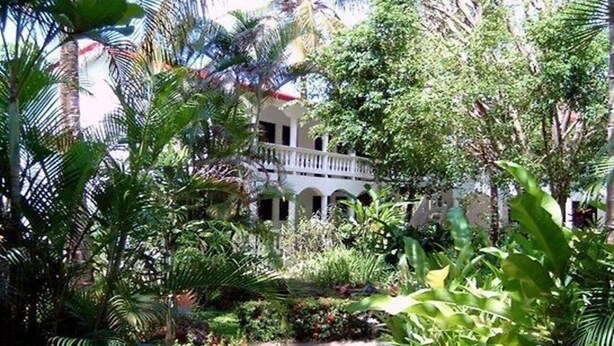 Un jardin luxuriant avec un bâtiment blanc doté d’un balcon.