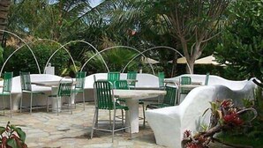 Une terrasse extérieure avec des tables blanches et des chaises vertes, entourée d’une végétation luxuriante et de palmiers.