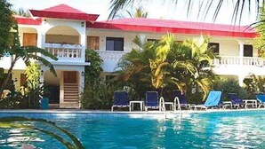 Un bâtiment à deux étages, doté d’un toit rouge et d’un espace piscine avec des chaises longues.
