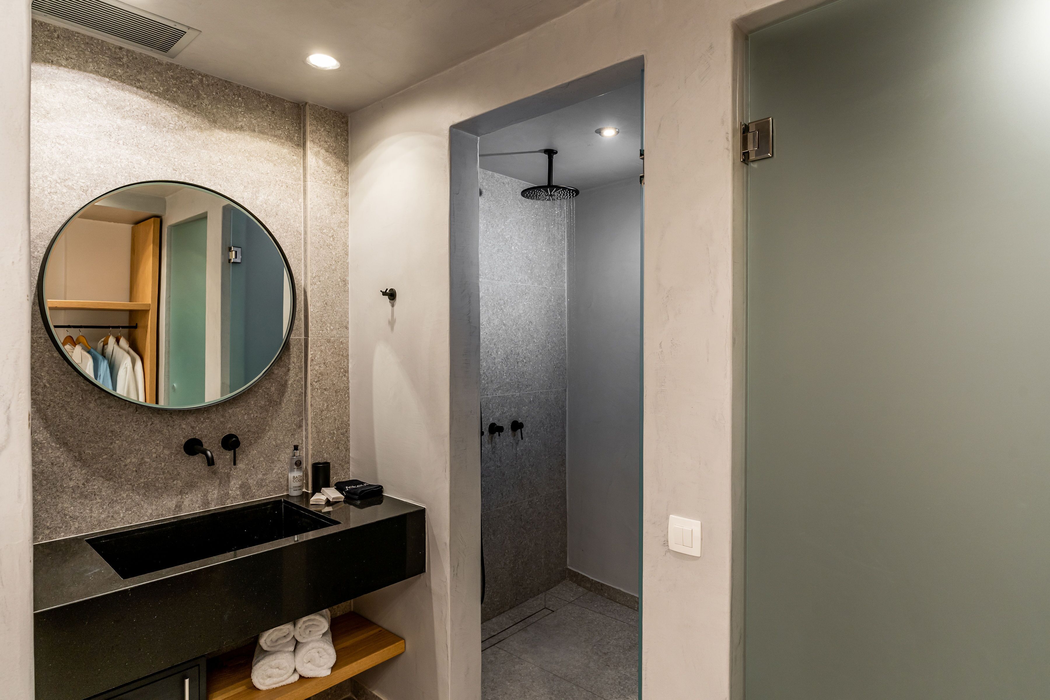 A modern bathroom with a round mirror, black sink, and a walk-in shower.