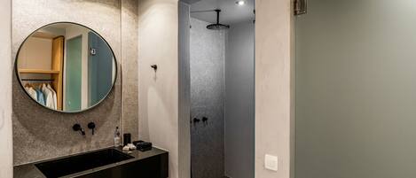 A modern bathroom with a round mirror, black sink, and a walk-in shower.