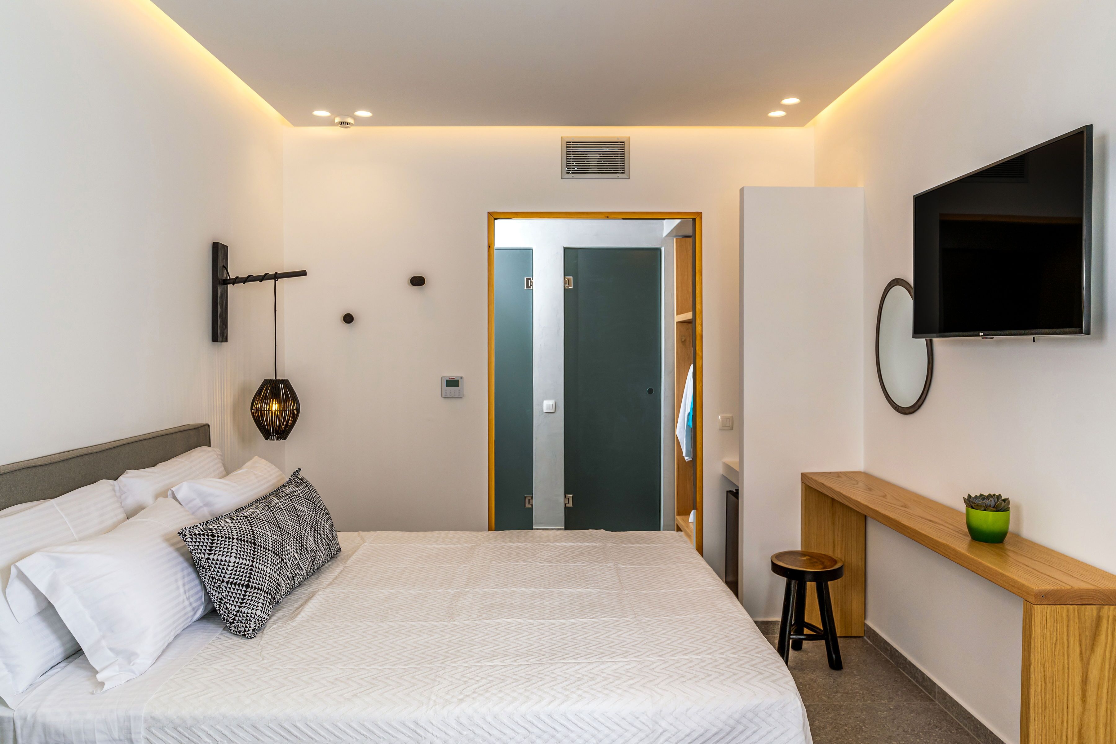 A modern hotel room with a neatly made bed, a wooden desk, a television, and a mirror on the wall.