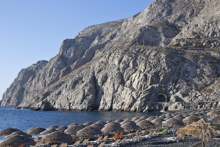 A rocky coastline with a beach area featuring sun loungers and thatched umbrellas.