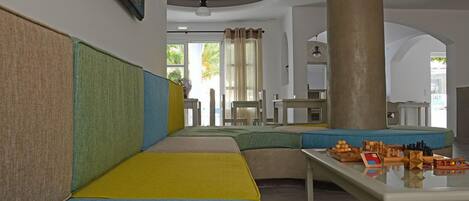 A hotel lobby with a long, curved seating area with colorful cushions, a central pillar, and a table with board games.