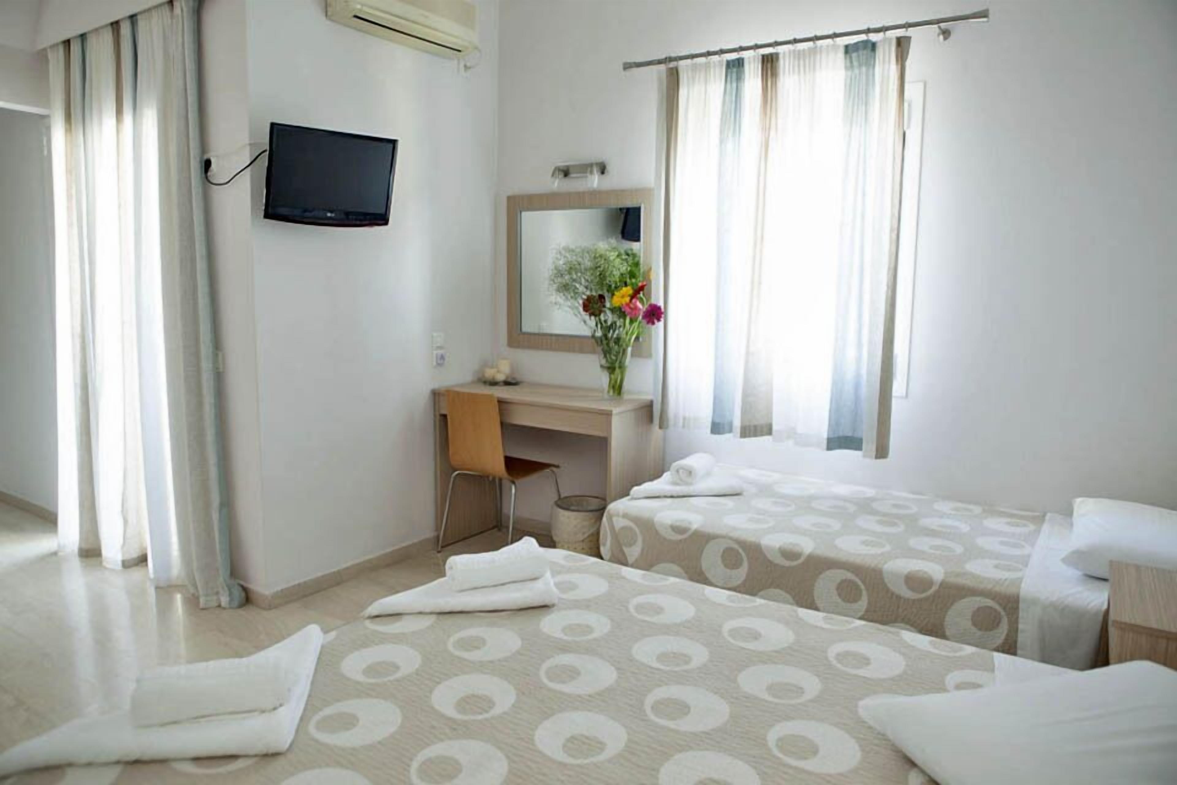 A hotel room with two beds, a desk, a TV, a mirror, and a window with curtains.