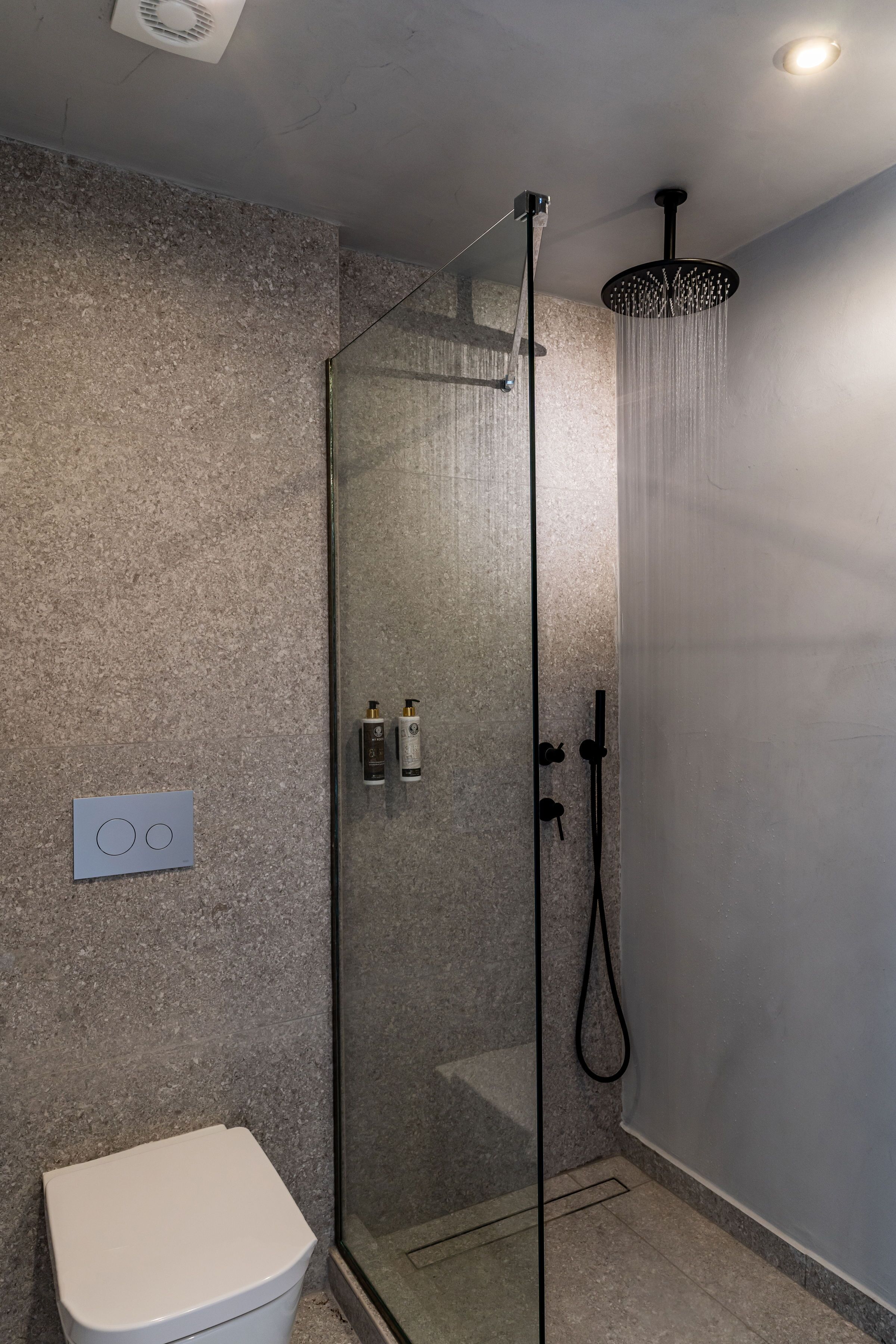 A modern bathroom with a glass-enclosed shower, a white toilet, and a control panel on the wall.