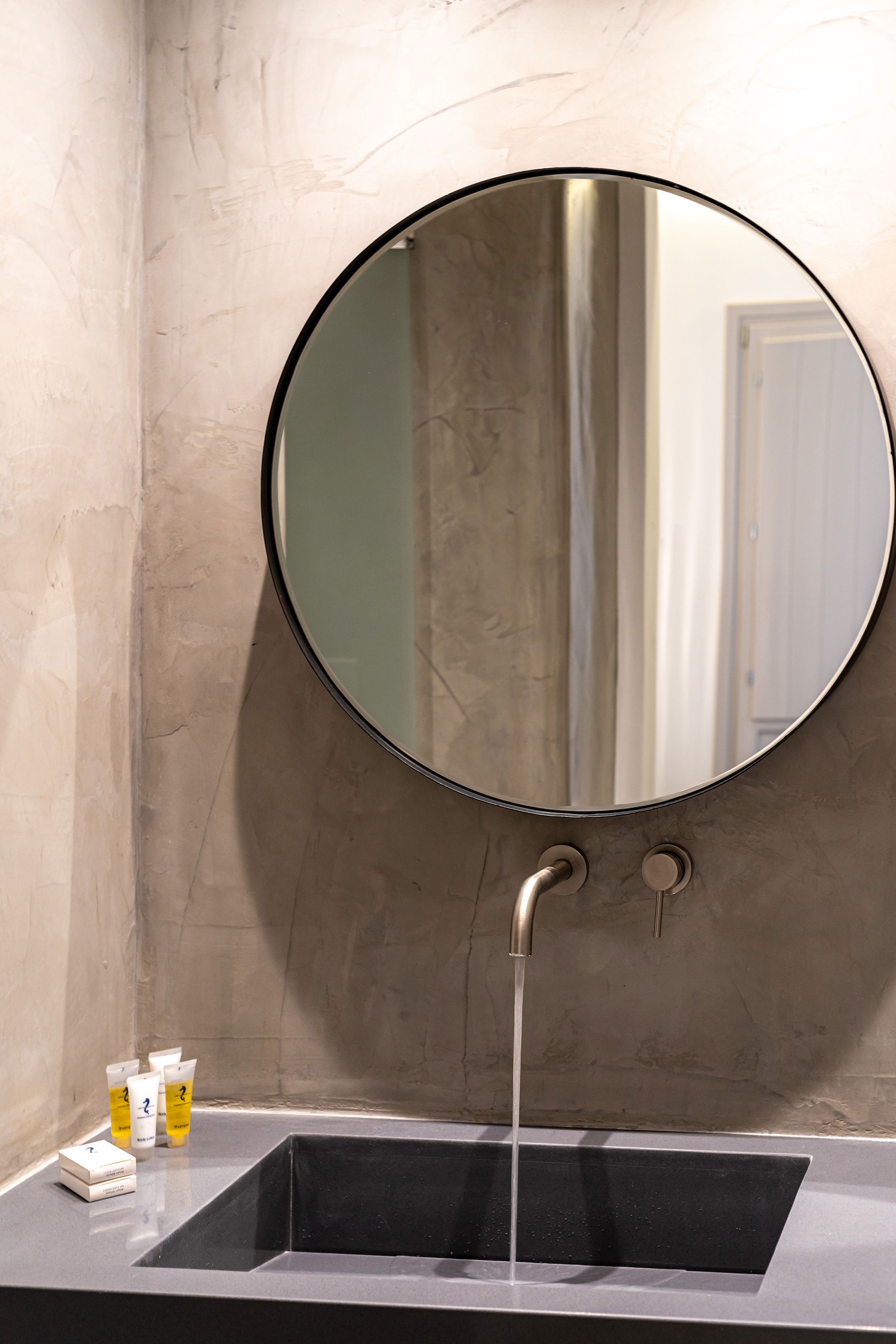 A bathroom with a round mirror, a sink, and toiletries.