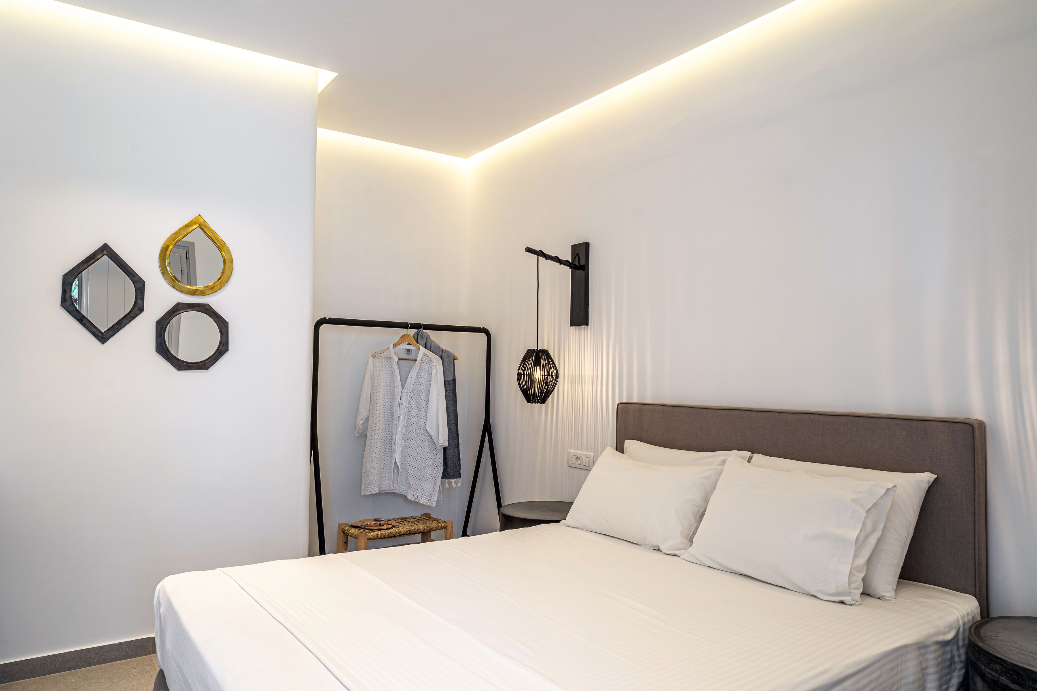Una habitación de hotel moderna con una cama bien hecha, un perchero de pared y un espejo de diseño geométrico original.