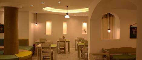 A cozy, well-lit dining area with round tables and chairs, a large pillar, and a curved seating area.