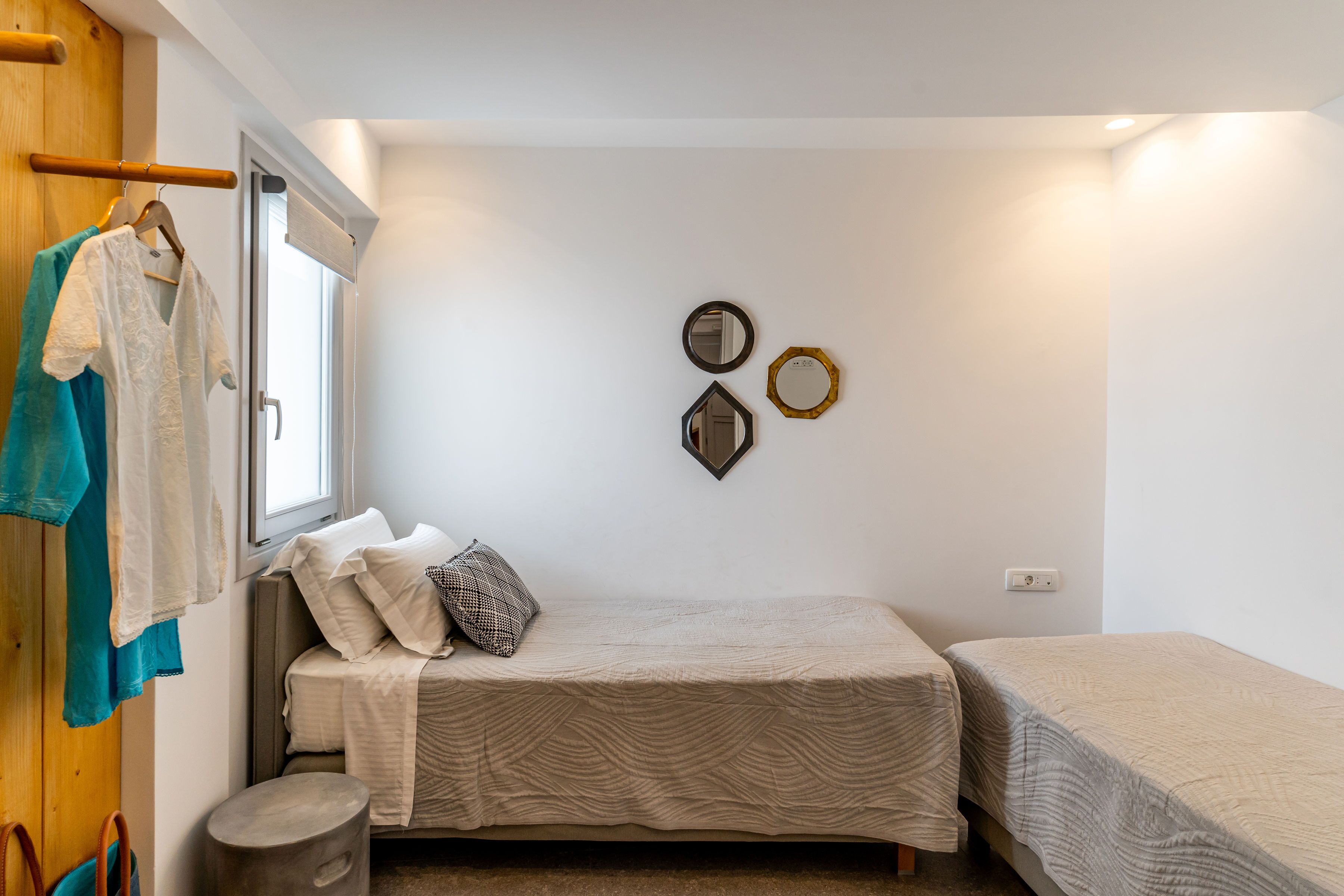 A compact bedroom with a single bed, a small stool, and a window.