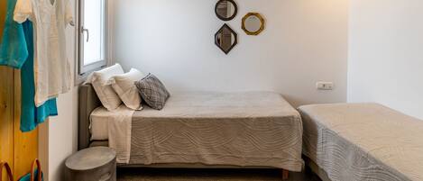 A compact bedroom with a single bed, a small stool, and a window.