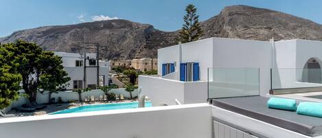 A rooftop terrace with a pool, white buildings, and a mountain in the background.