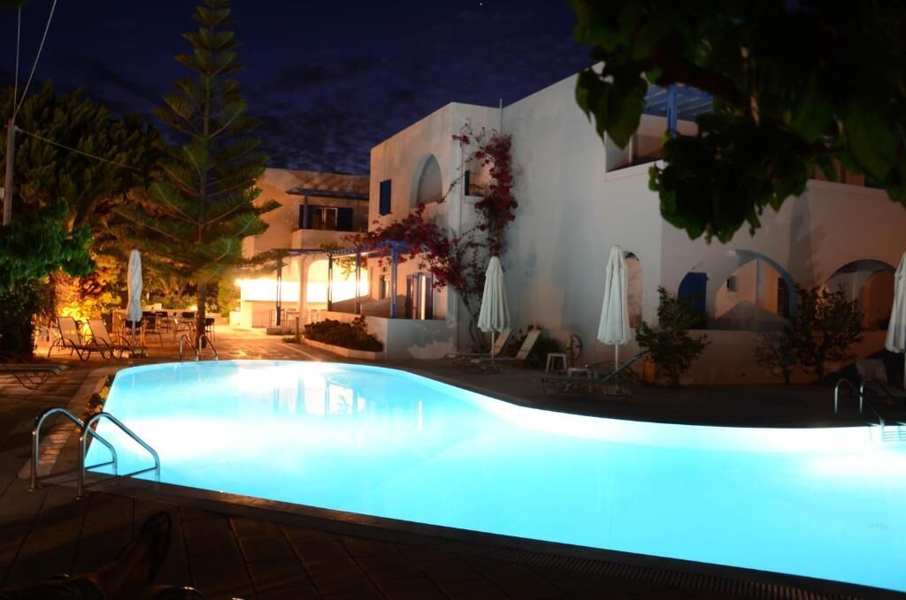 A swimming pool with lounge chairs and umbrellas, surrounded by a building with arches and a night sky.