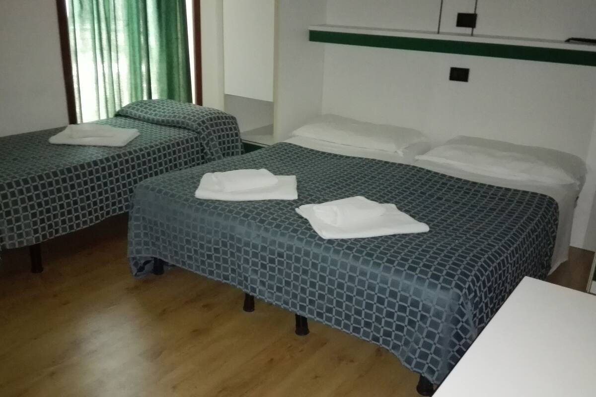 A hotel room with two single beds, each with a patterned bedspread and white pillows. There is a small table and a green-framed mirror on the wall.