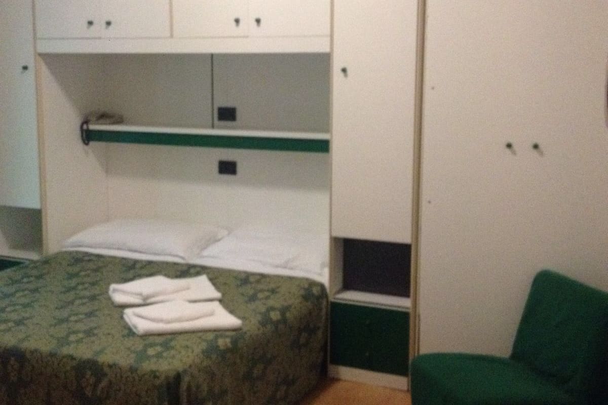 A room with a bed, a green chair, and a wardrobe with multiple compartments.