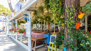 Un espace extérieur accueillant, aménagé avec des tables et des chaises, et entouré d’une végétation luxuriante et de plantes suspendues.