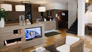 A modern hotel lobby with a reception desk, television, wicker furniture, and a staircase. - Hotel Majorca (Riccione)