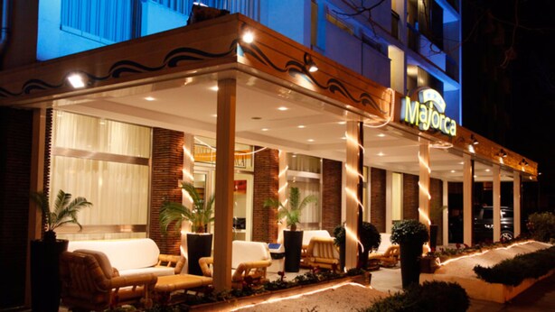 A hotel exterior with a covered outdoor seating area, potted plants, and a sign reading "Majorca". - Hotel Majorca (Riccione)