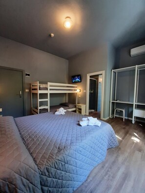 A bedroom with a large bed, a bunk bed, a TV, and a wardrobe. - Hotel Alabama (RIMINI)