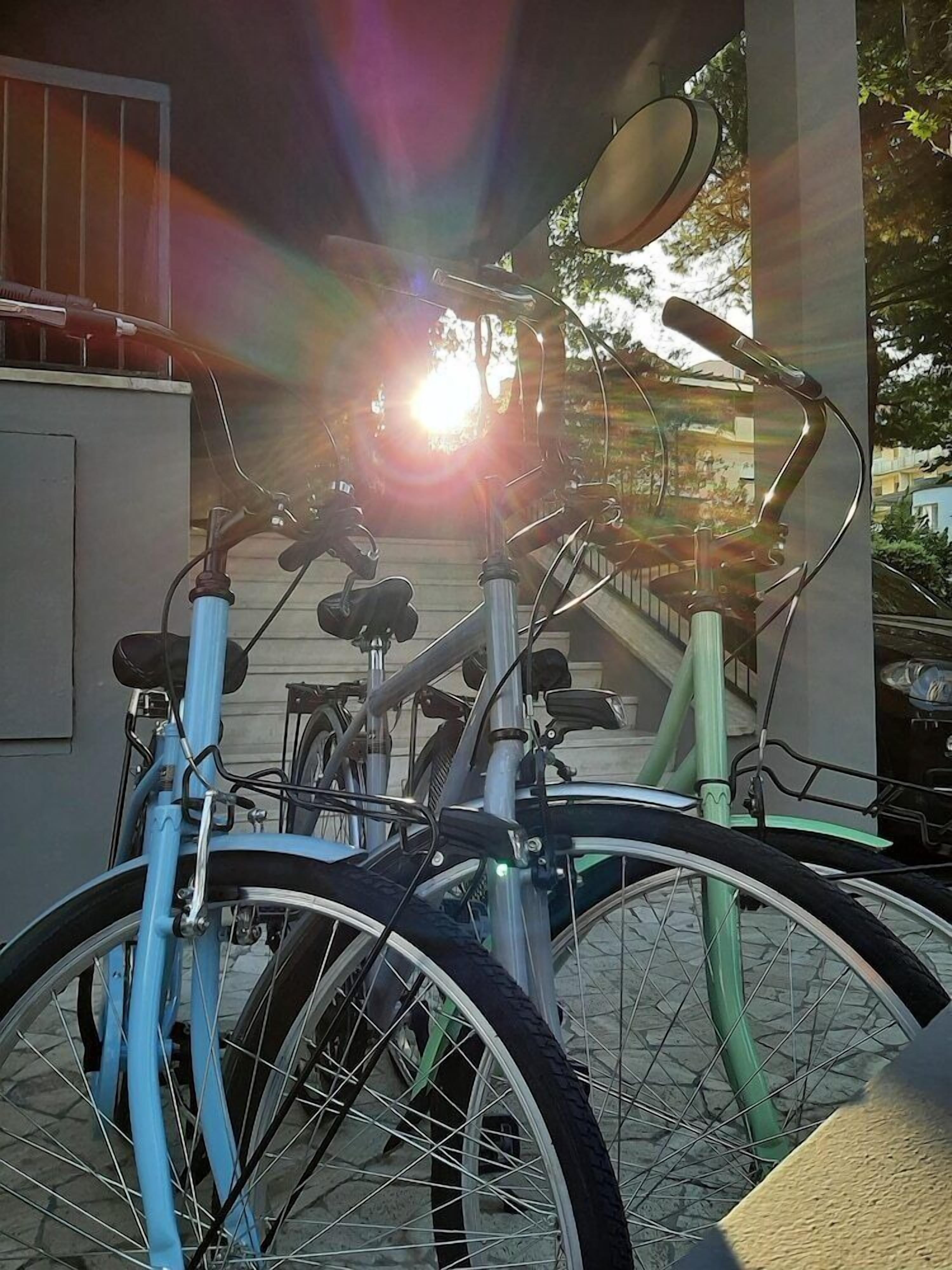 A bicycle parked under a structure with a sun shining through, casting light and shadow.
