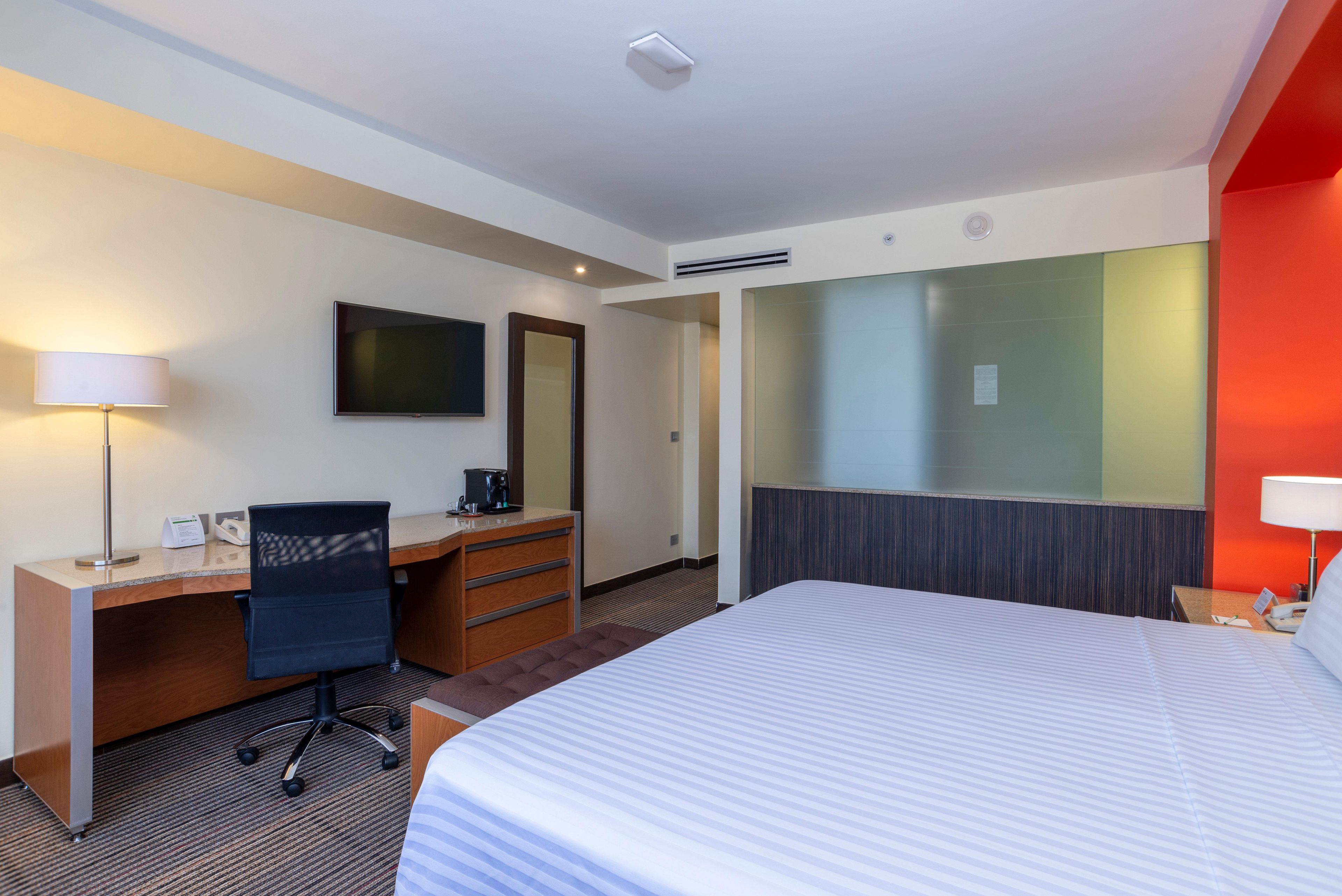A hotel room with a bed, desk, chair, and a television on the wall.