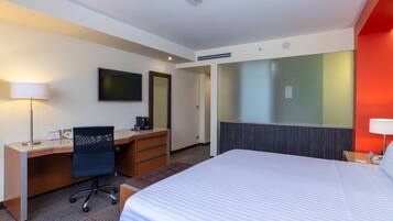 A hotel room with a bed, desk, chair, and a television on the wall.