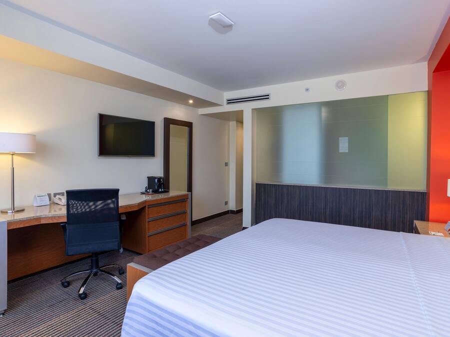 A hotel room with a bed, desk, chair, and a television on the wall.