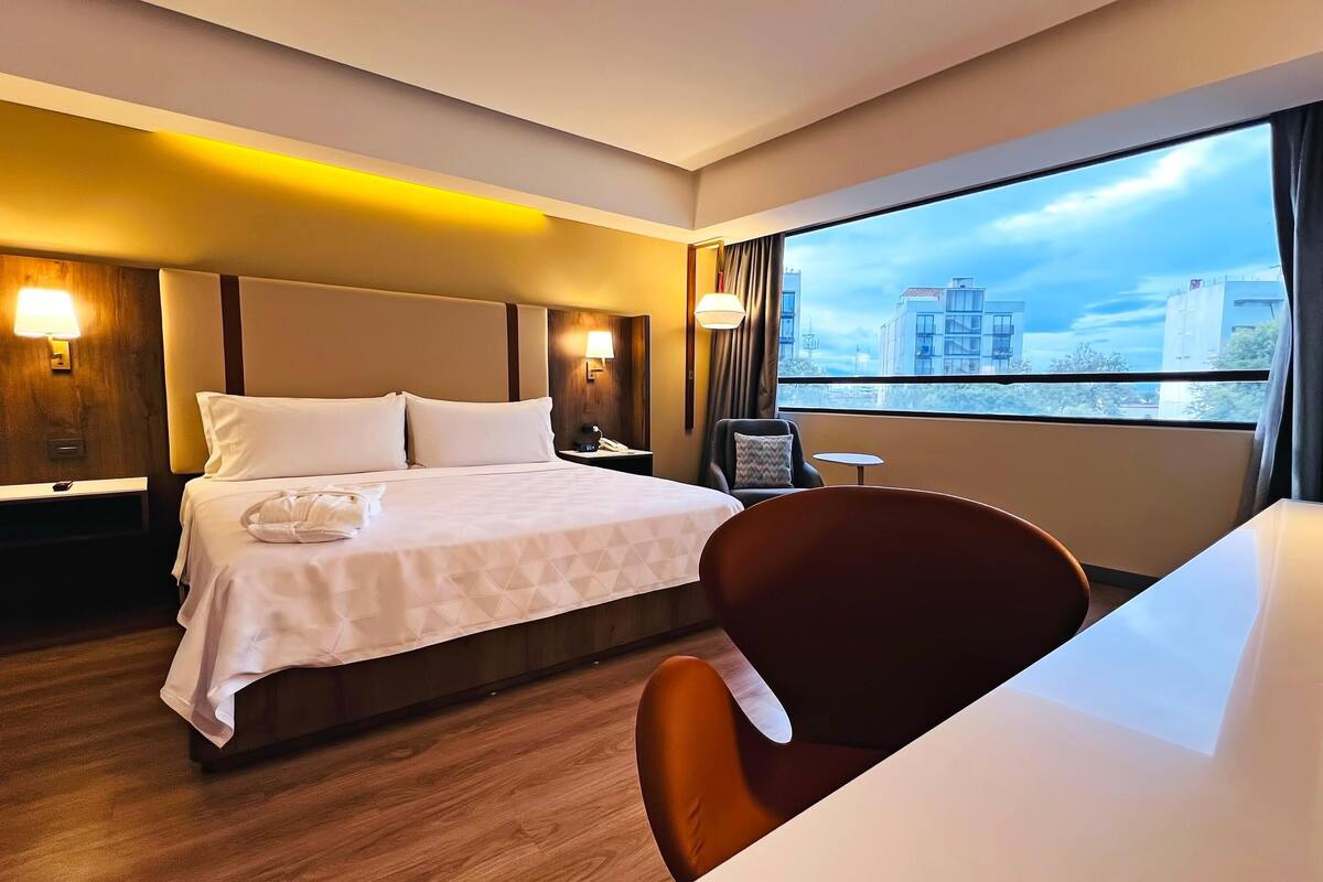 A hotel room with a bed, bedside tables, a desk, and a chair.