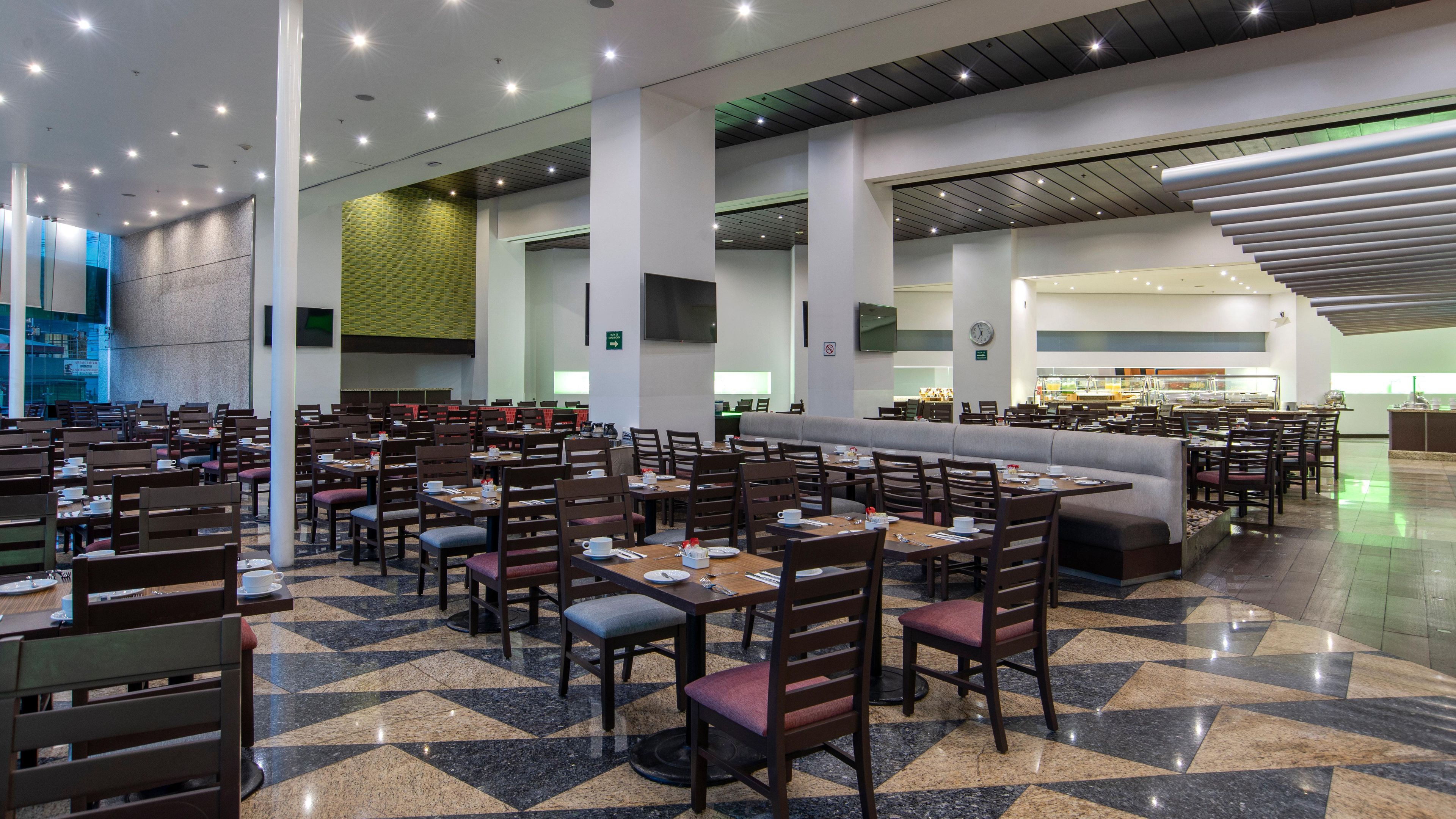 A spacious dining area with multiple tables and chairs, a large seating area, and a kitchen in the background.