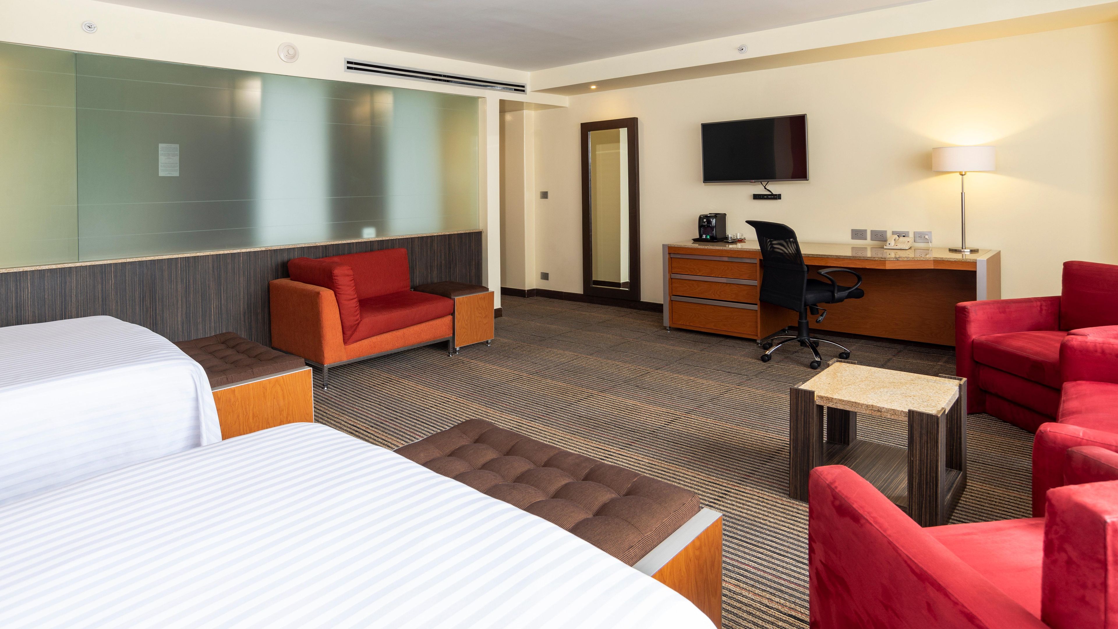 Habitación de hotel con cama, sofá, escritorio, silla, televisor y lámpara.