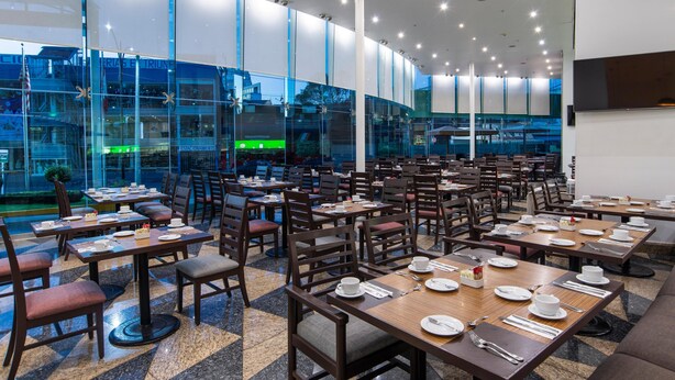 Een restaurant met meerdere tafels en stoelen, grote ramen en uitzicht op buiten.