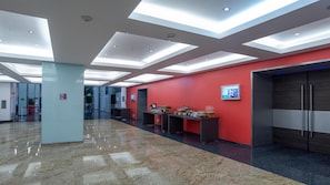 En moderne lobby med en rød accentvæg, en receptionsdisk og et digitalt informationsskilt.