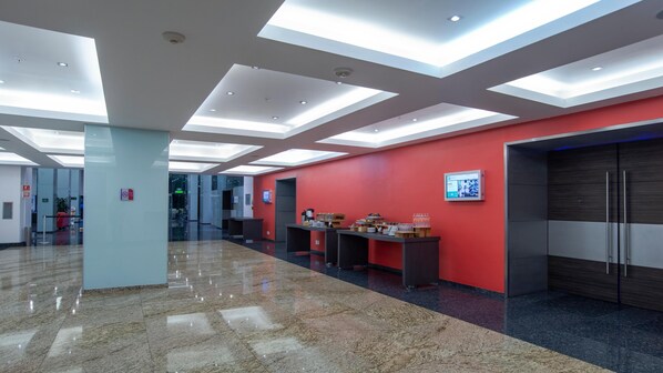 A modern lobby with a red accent wall, a reception desk, and a digital information board.