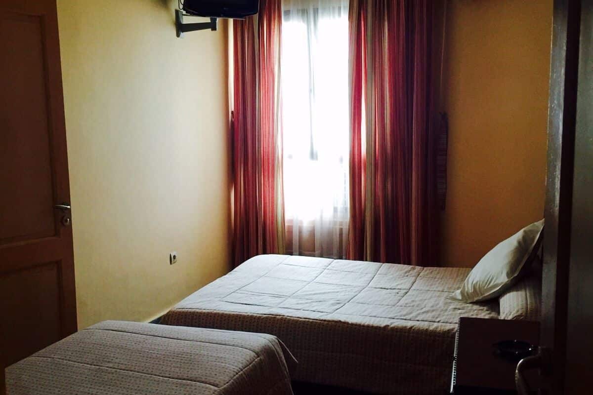 Een kamer met twee bedden, een aan de muur bevestigde televisie en een airconditioning.