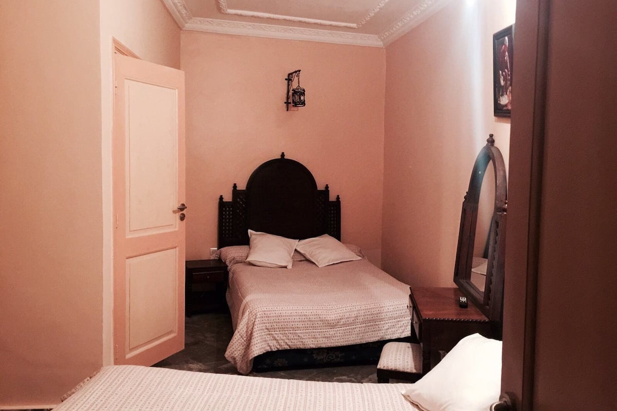 Een slaapkamer met een tweepersoonsbed, nachtkastje, spiegel en een deur.