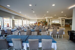 Un comedor amplio con varias mesas y sillas, ventanas grandes y una barra central.