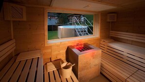Et saunaområde med træbænke, et vindue med udsigt til en hottub udenfor, og en stenbænk med rød belysning.