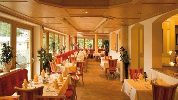 En restaurant med lange borde, røde polstrede stole og krukkeplanter.