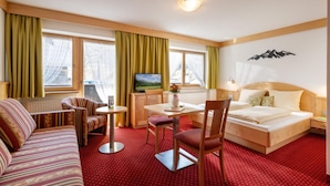 A hotel room with a bed, a sofa, a dining table, and a TV. - Eggerwirt (SÖLL)