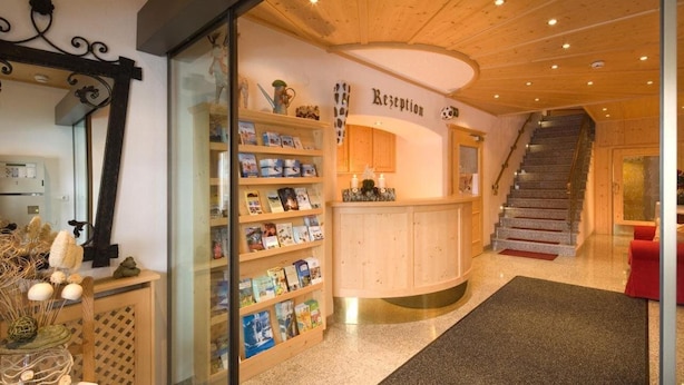 A reception area with a wooden reception desk, a staircase, and a glass partition with bookshelves. - Eggerwirt (SÖLL)