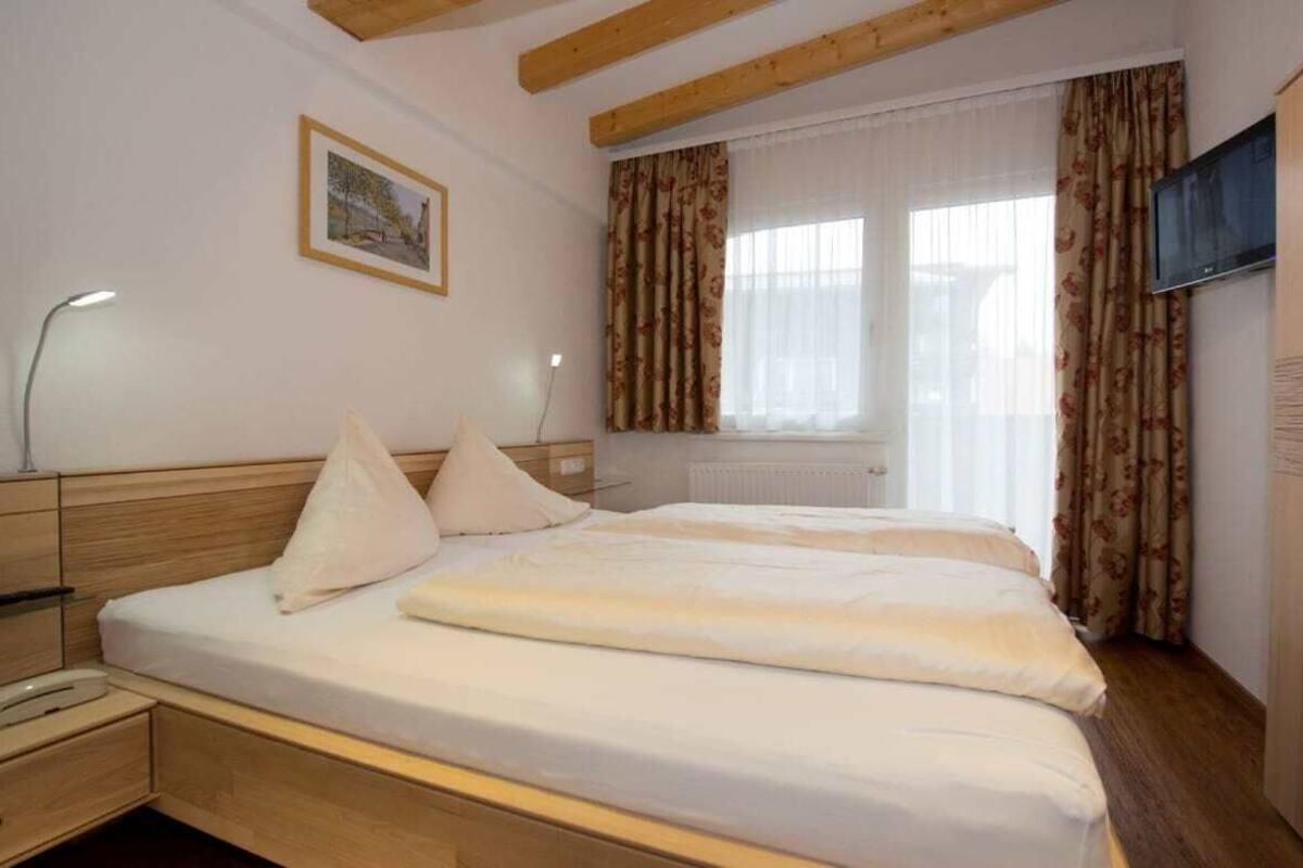 A hotel room with a bed, a bedside table, a lamp, a TV, and a window with curtains.