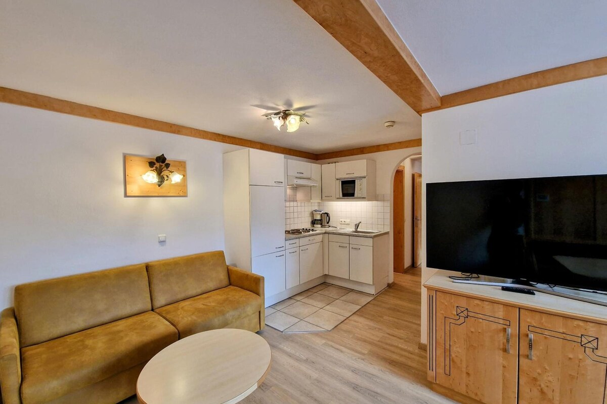 A compact living space with a sofa, a small round table, a kitchenette, and a television.