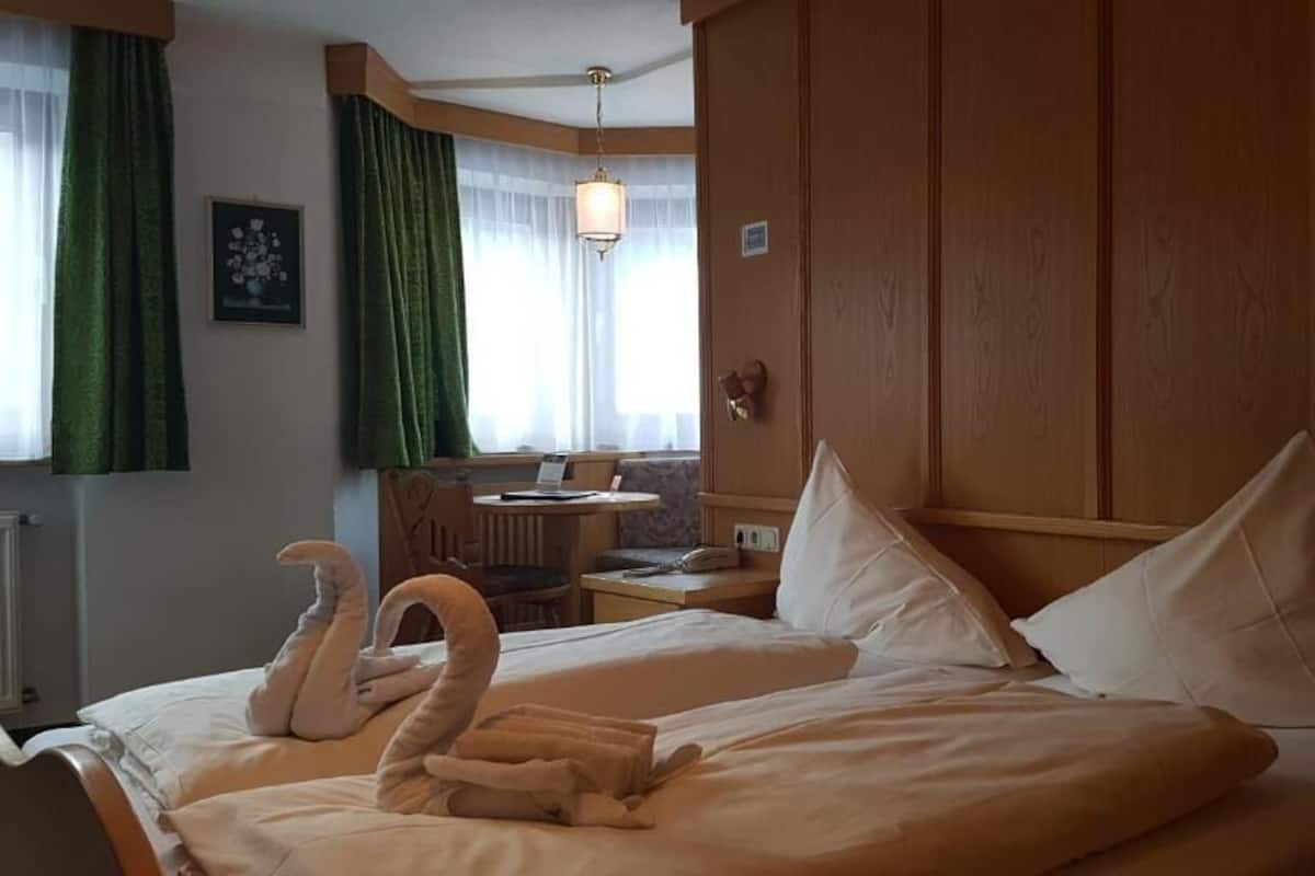 A hotel room with a bed featuring swan-shaped towels, a wooden headboard, and a nightstand with a lamp.