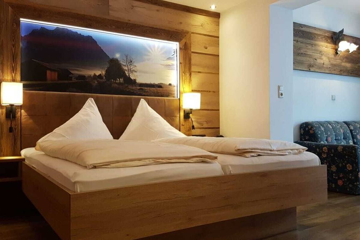 A wooden bed with white bedding, two bedside lamps, a large framed picture on the wall, and a floral sofa in a room with wooden paneling.