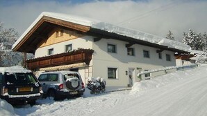 A two-story chalet with a sloped roof, wooden exterior, and a snow-covered ground. - Gerlinde Feichter (Soell)