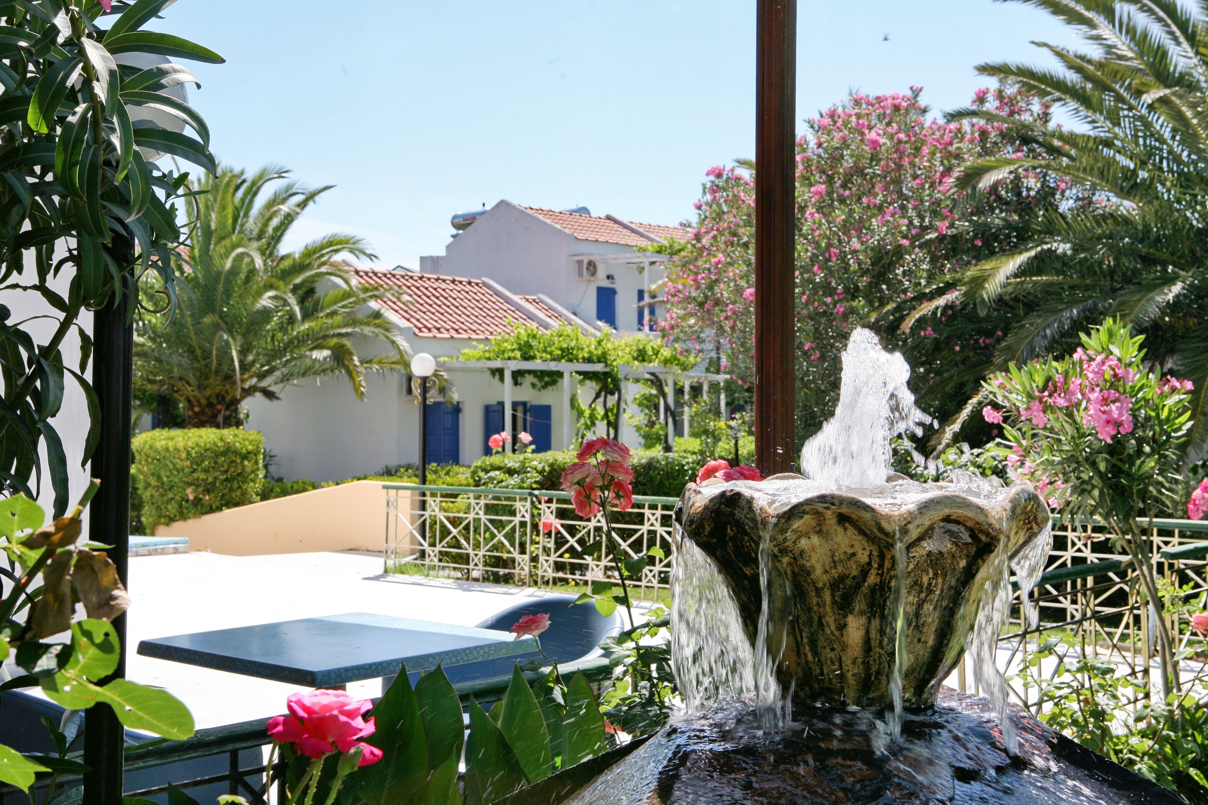 A fountain in a garden with a pool and a building in the background.
