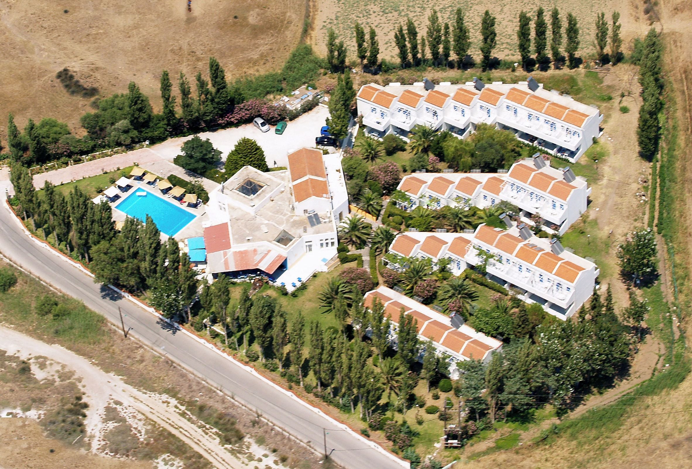 An aerial view of a residential area with multiple white buildings, a swimming pool, and surrounding greenery.