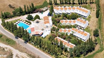 An aerial view of a residential area with multiple white buildings, a swimming pool, and surrounding greenery.
