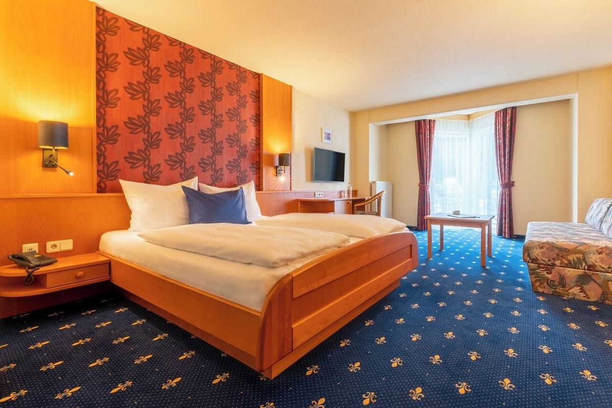 Quarto de hotel com uma cama grande, uma escrivaninha, uma cadeira, uma mesinha e uma televisão.